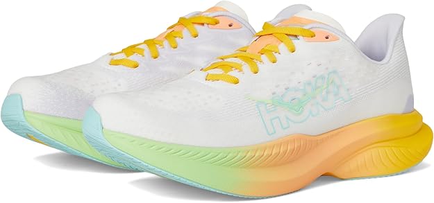 Un paio di scarpe da ginnastica Hoka Mach 6 bianche con lacci gialli e suole multicolori con sfumature verdi, gialle e blu. Il logo Hoka è leggermente visibile sul lato.