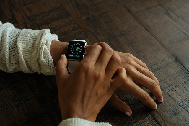 Una persona che indossa un maglione bianco utilizza uno smartwatch Suunto al polso sinistro, che visualizza informazioni sul fitness tracking, su un tavolo di legno.